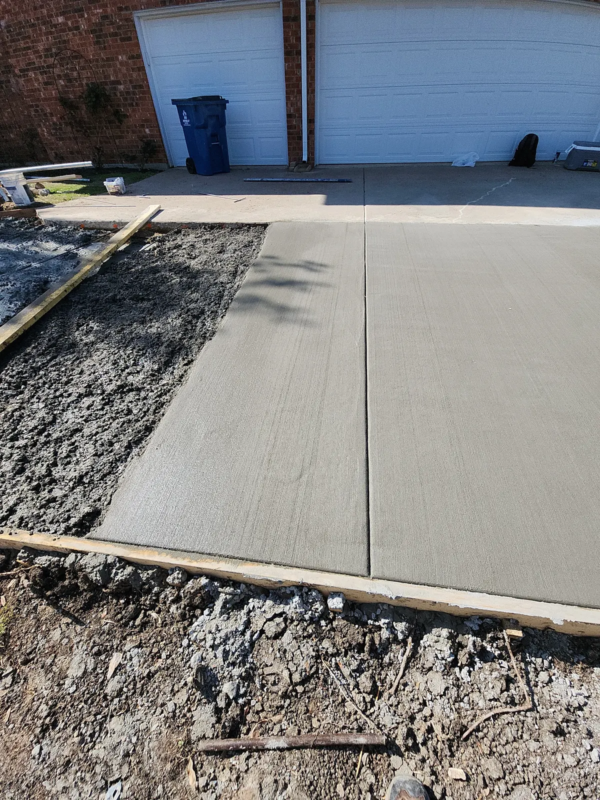 Freshly finished driveway section beside concrete still being placed inside wood forms
