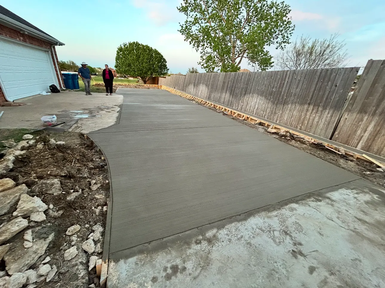 Long freshly poured driveway running along a wood fence to a side-entry garage