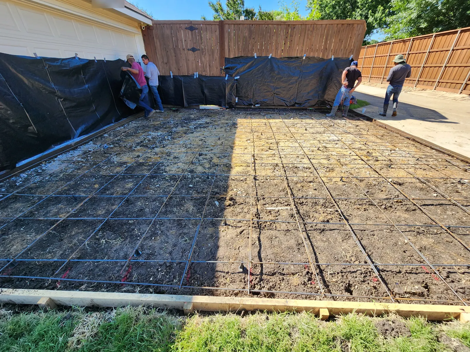 Crew finishing rebar layout in a driveway with walls protected by plastic