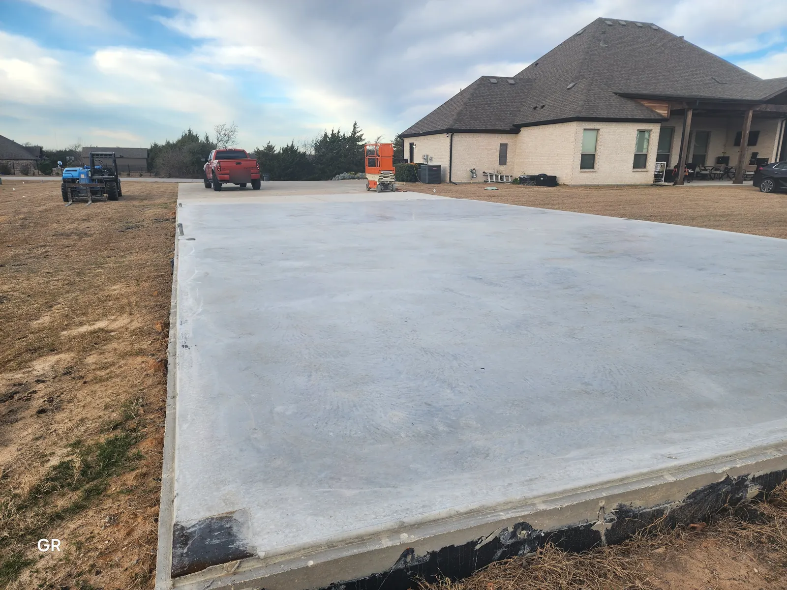 Large concrete slab poured for a metal shop beside a brick home