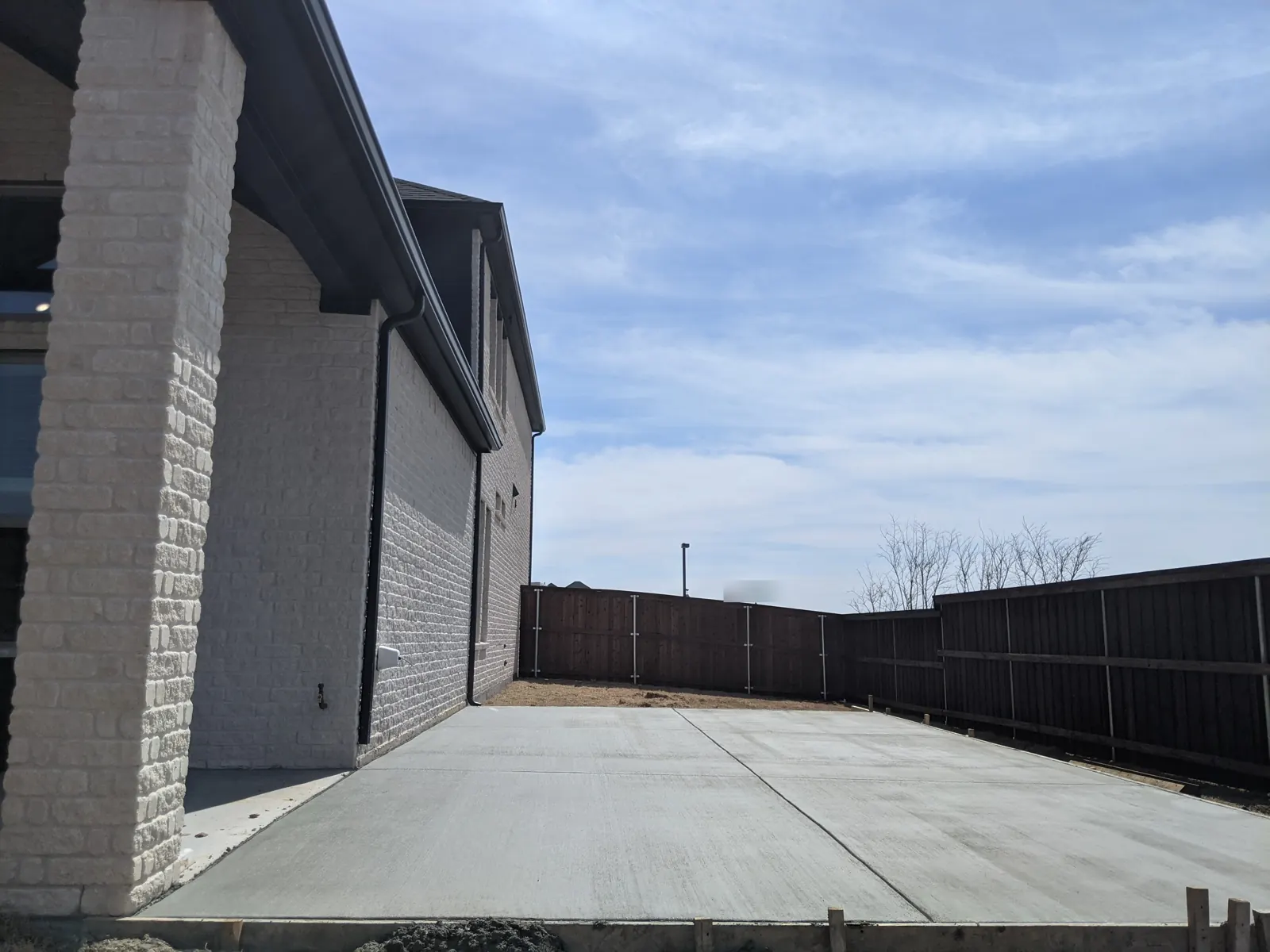 New concrete side slab along a two-story home and fence line