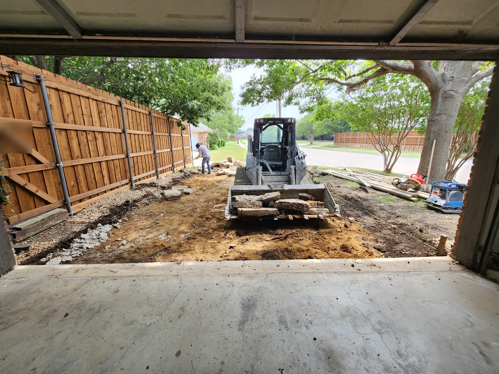Skid steer hauling broken-out driveway concrete, seen from inside the garage