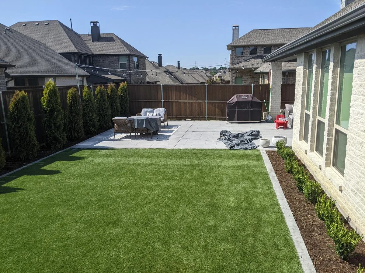 Large paver patio with a manicured artificial-turf lawn and boxwood border along the home