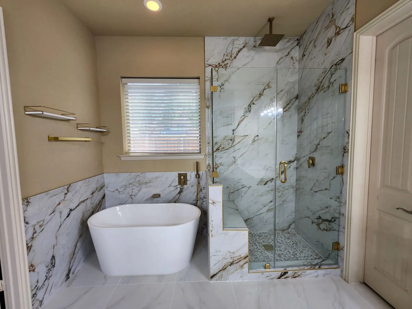 Marble-clad walk-in shower with brushed gold fixtures beside a freestanding tub