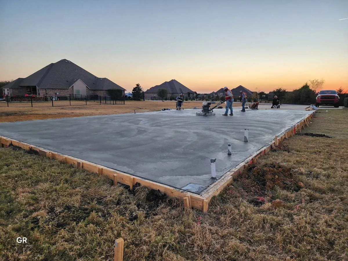 Crew power-troweling a freshly poured concrete slab at sunset