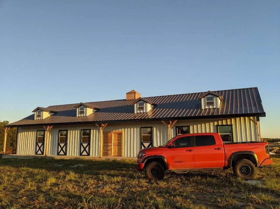 White metal barndominium with dark metal roof and dormers at sunset