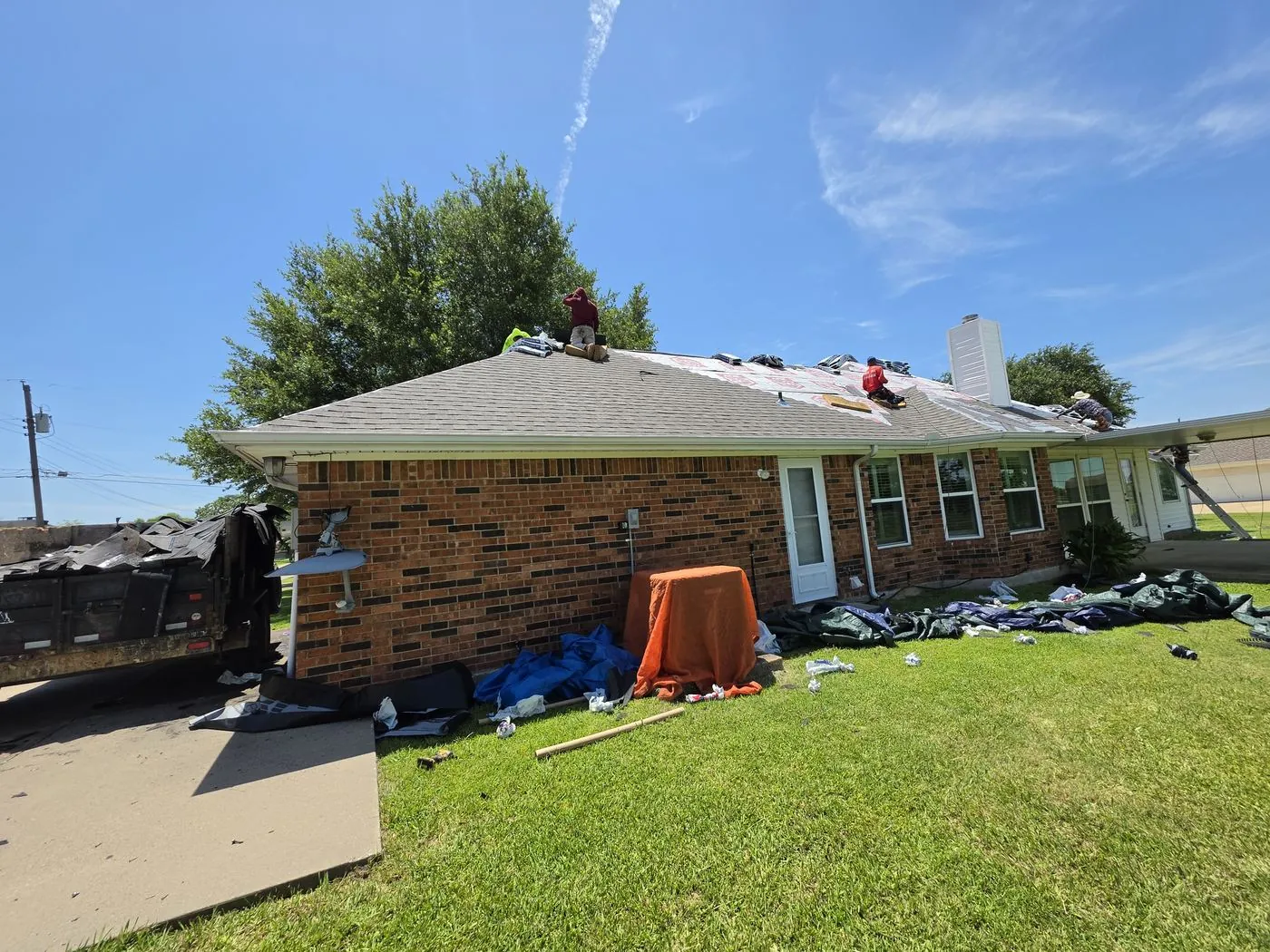 Roofing crew tearing off old shingles with a debris trailer staged on the driveway
