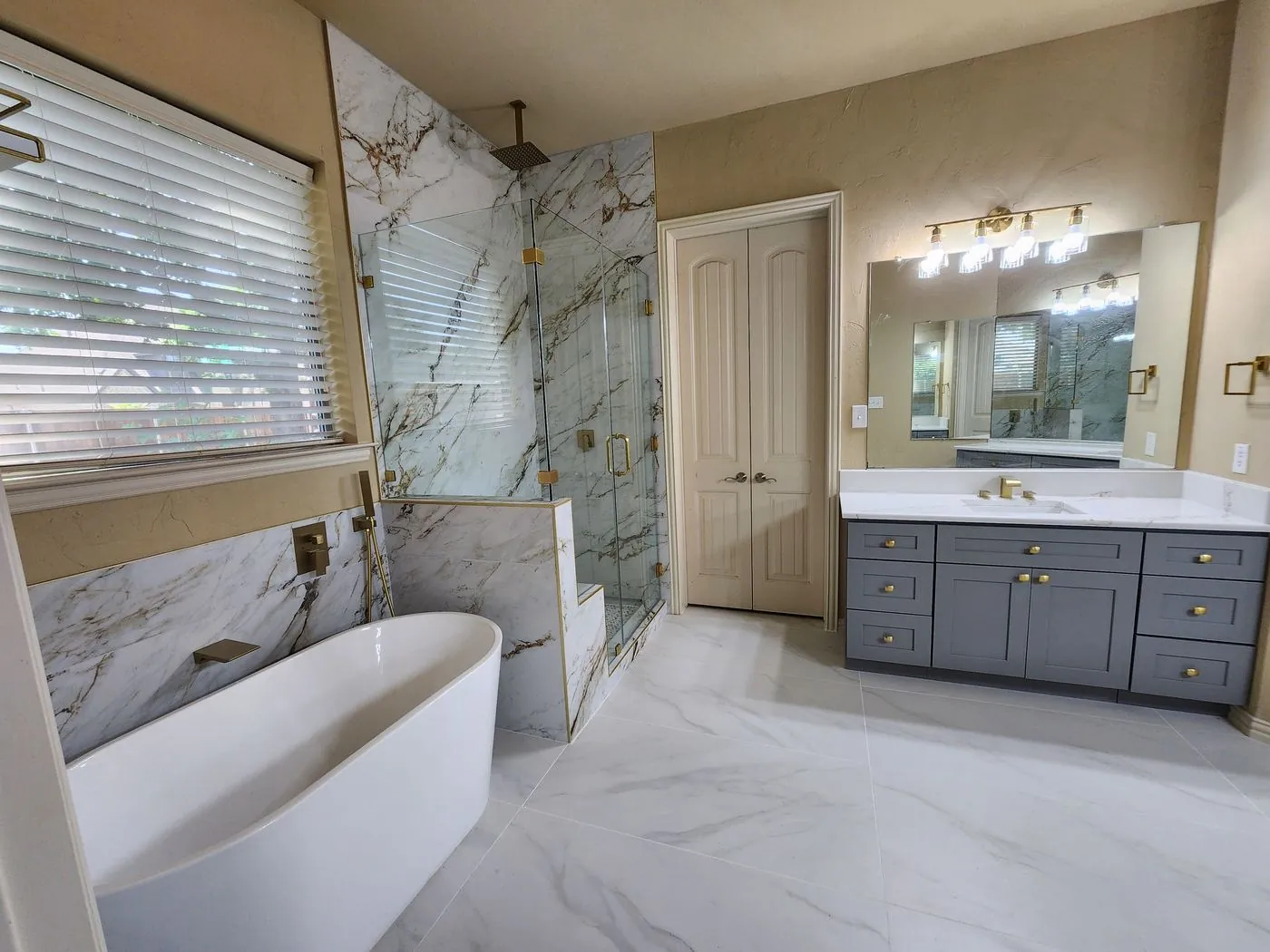 Remodeled master bathroom with gold-veined marble, freestanding soaking tub, glass shower and gray vanity