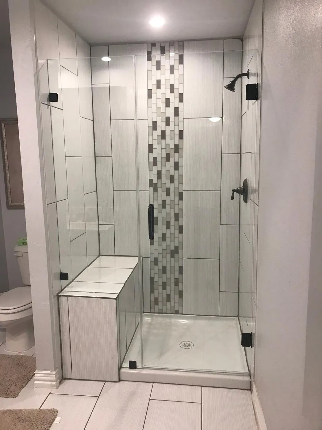 White tiled walk-in shower with a vertical glass mosaic accent stripe and built-in bench