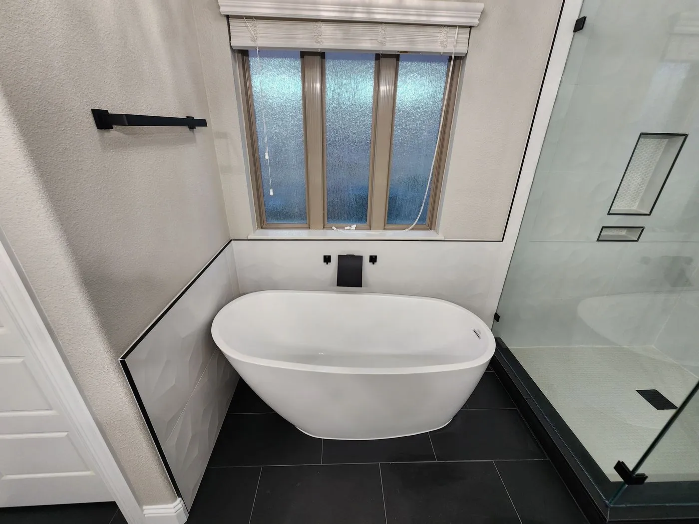 Freestanding tub with matte black filler and dark tile floor in a remodeled bathroom