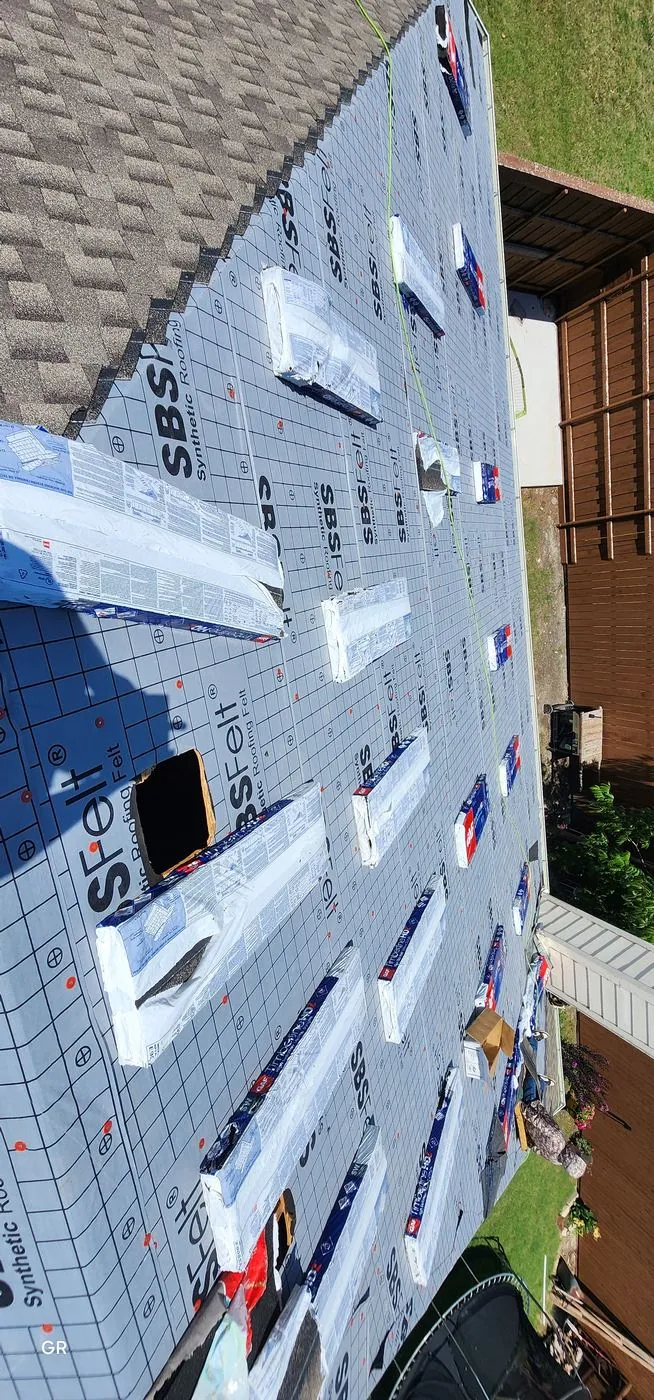 Roof deck covered in synthetic felt underlayment with new shingle bundles staged for installation