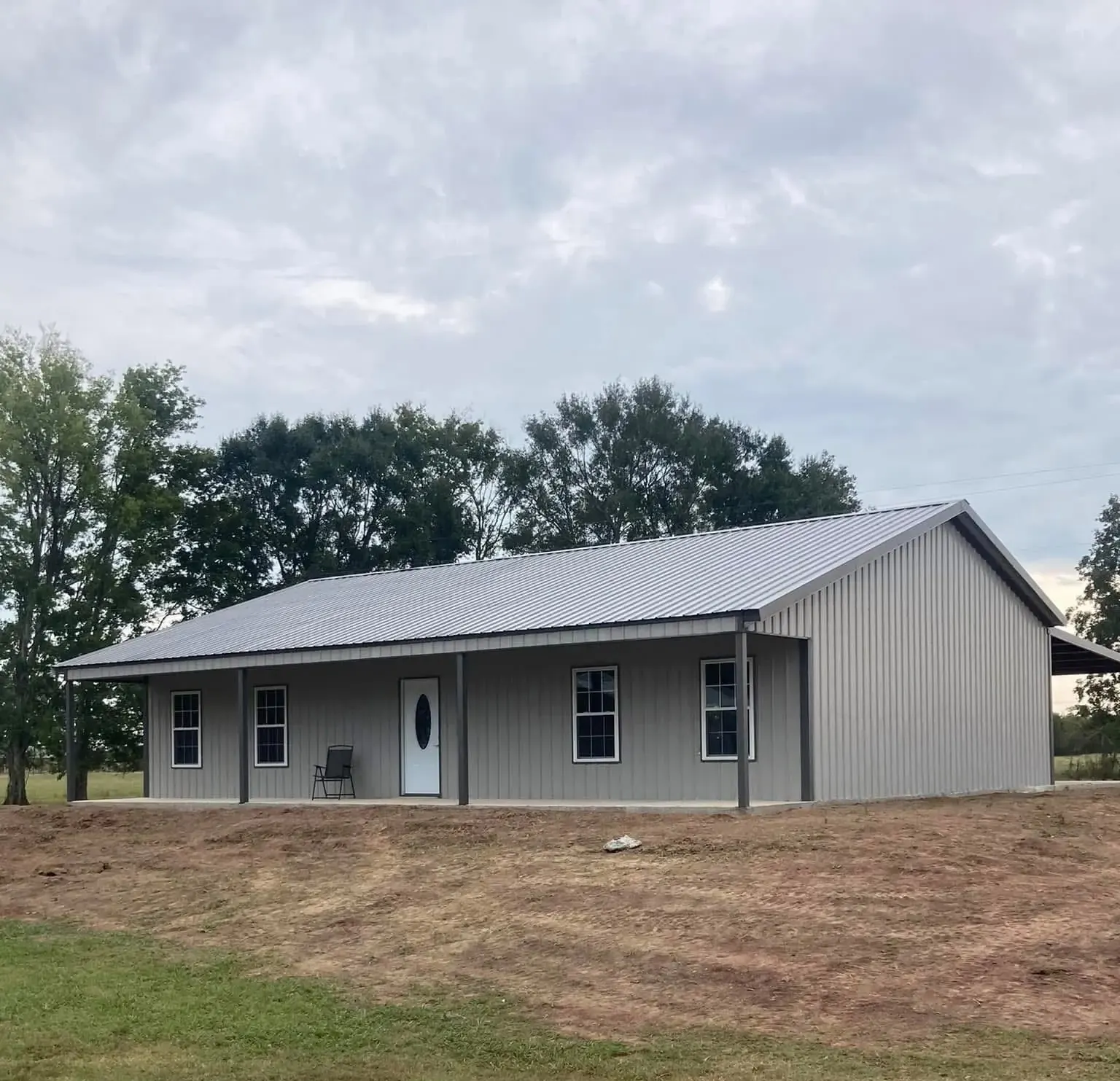 Gray metal building with windows, a front door and a full-length covered porch