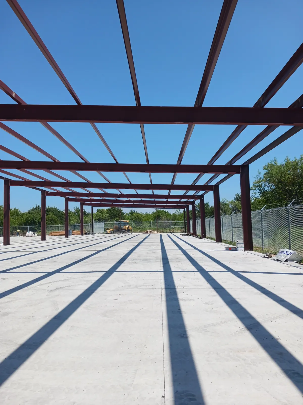 Red steel frame of a large metal building standing on a finished slab
