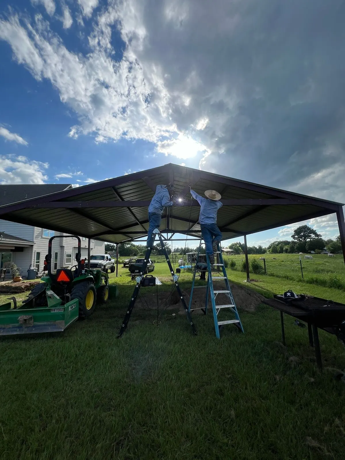 Two crew members on ladders welding the frame of a gable metal cover