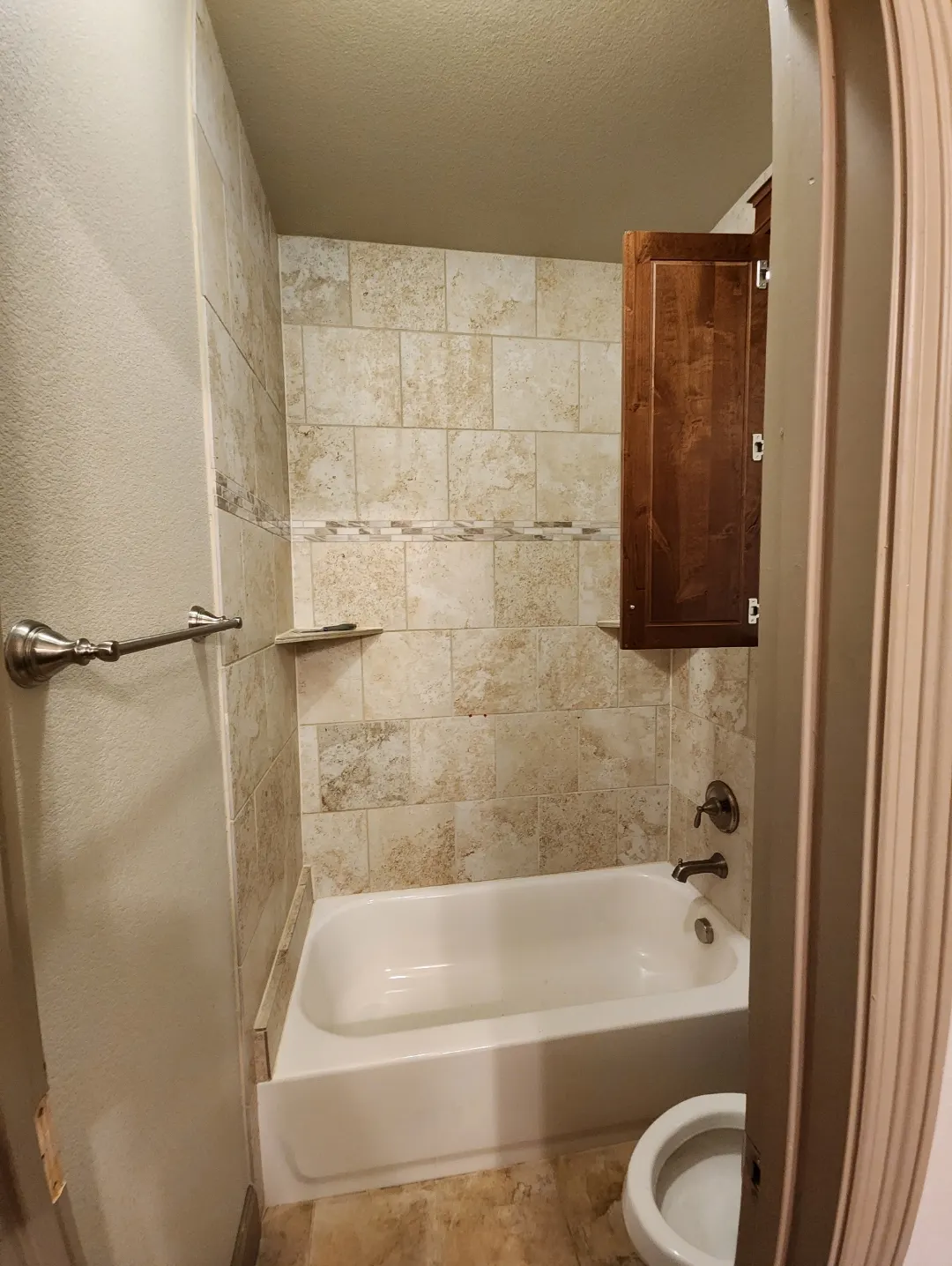 Before: Small bathroom with a standard tub and beige tile surround
