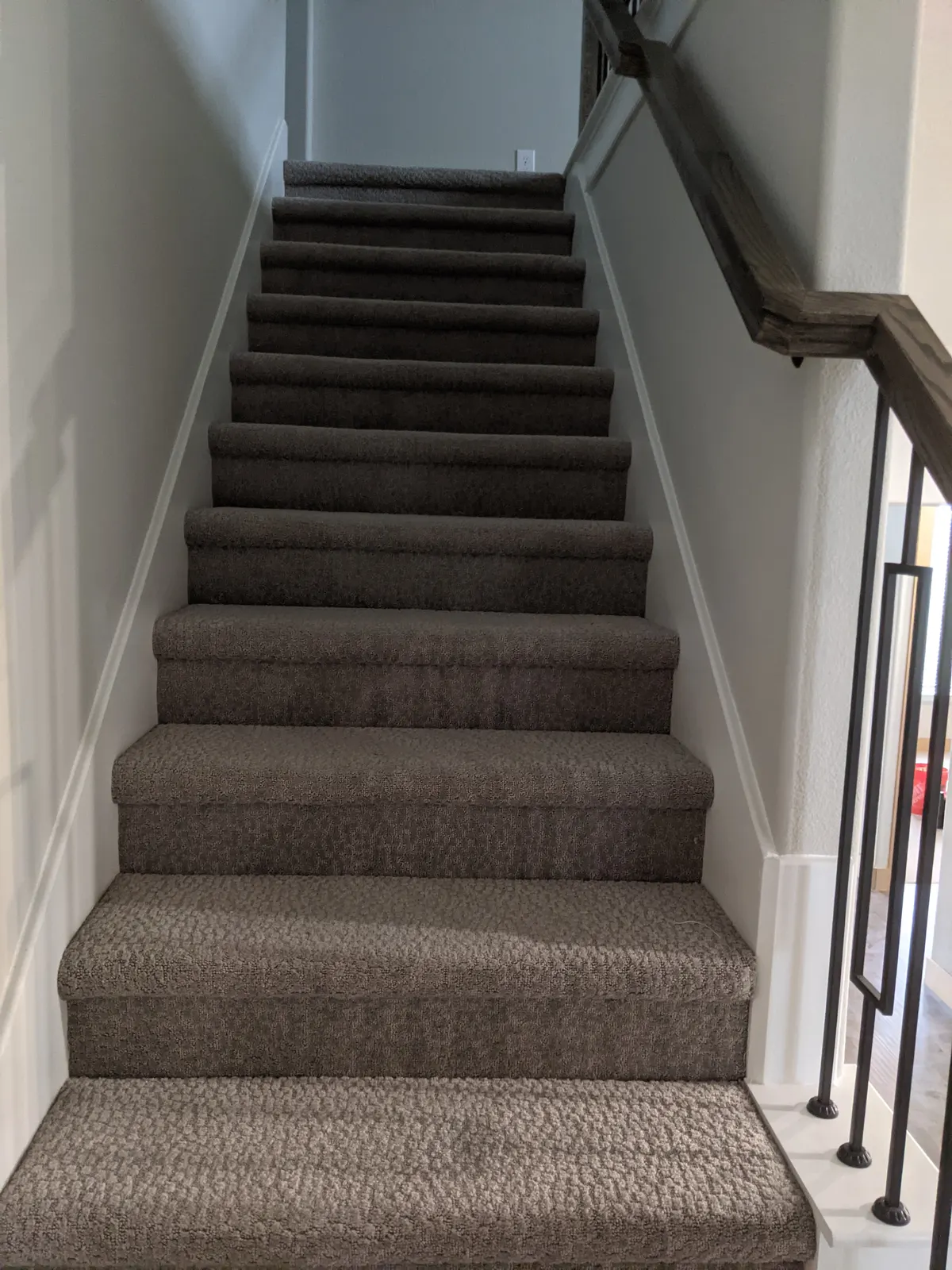 Before: Carpeted straight staircase with a wood handrail