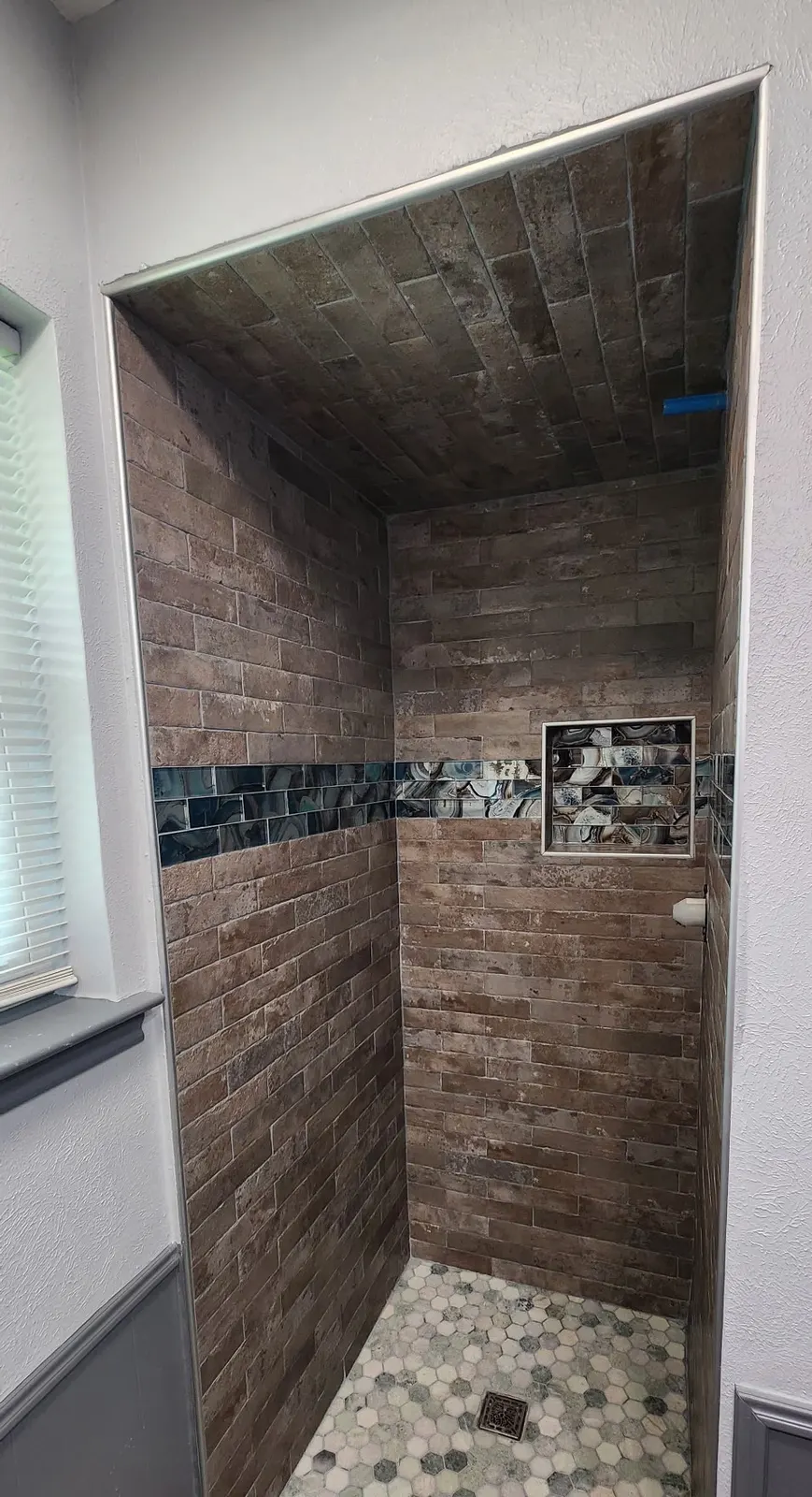In progress: Walk-in shower with brick-look tile ceiling and walls, a glass accent band and a matching niche, before glass is installed
