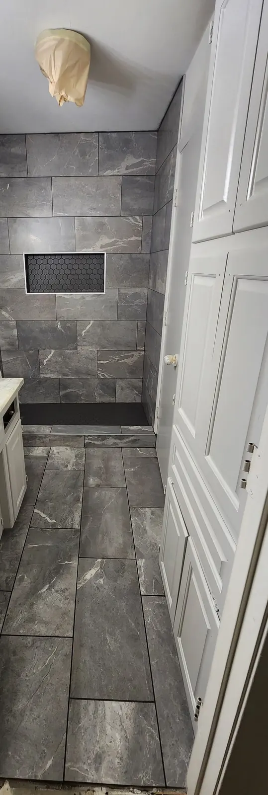 In progress: Gray marble-look walk-in shower with a black hexagon niche and matching floor, before trim-out