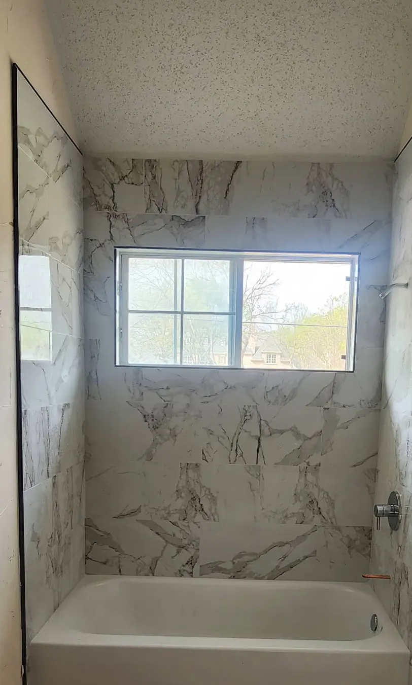 In progress: Tub surround tiled in large marble-look porcelain around a window, before fixtures are finished
