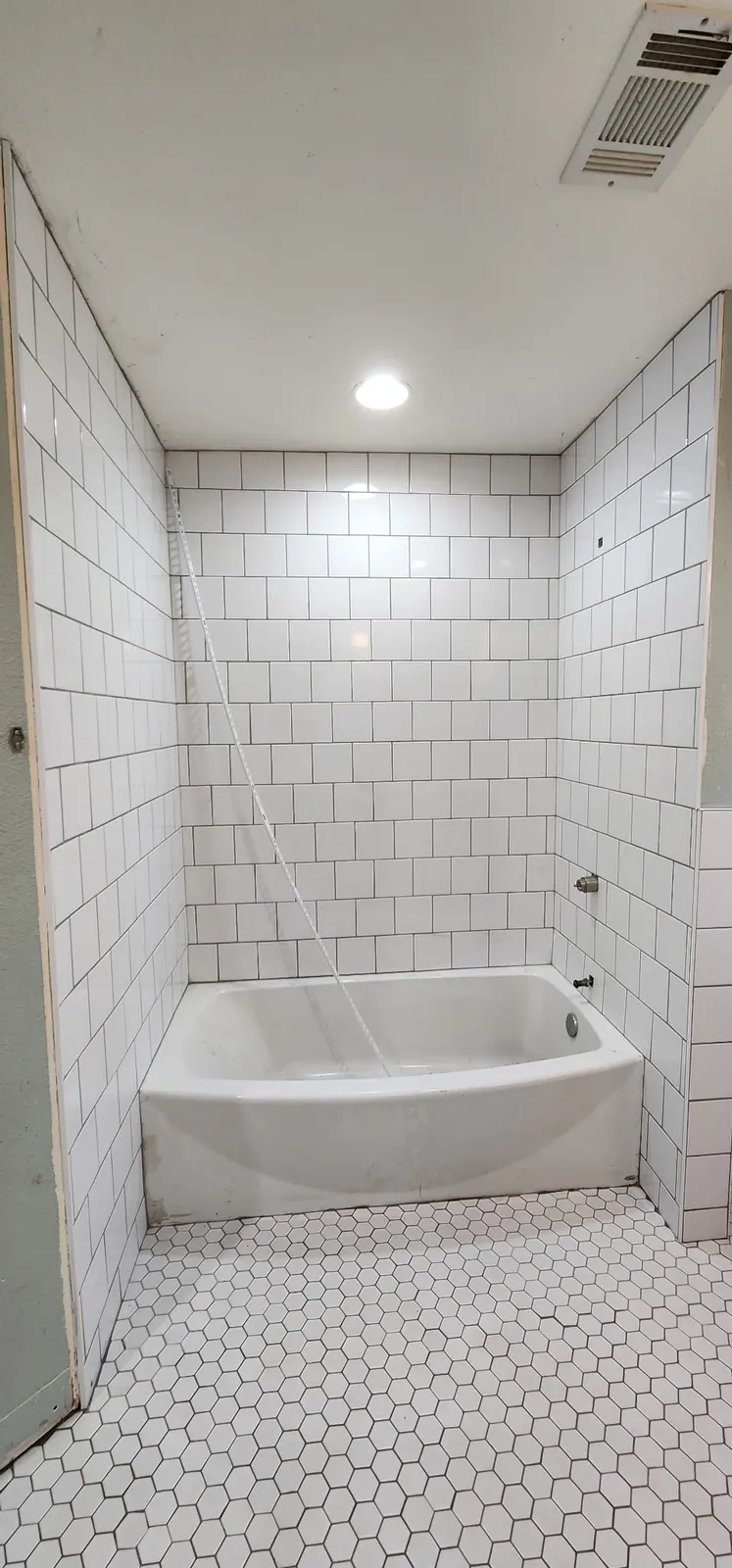 In progress: Tub surround in white square tile with a white hexagon mosaic floor, before trim-out