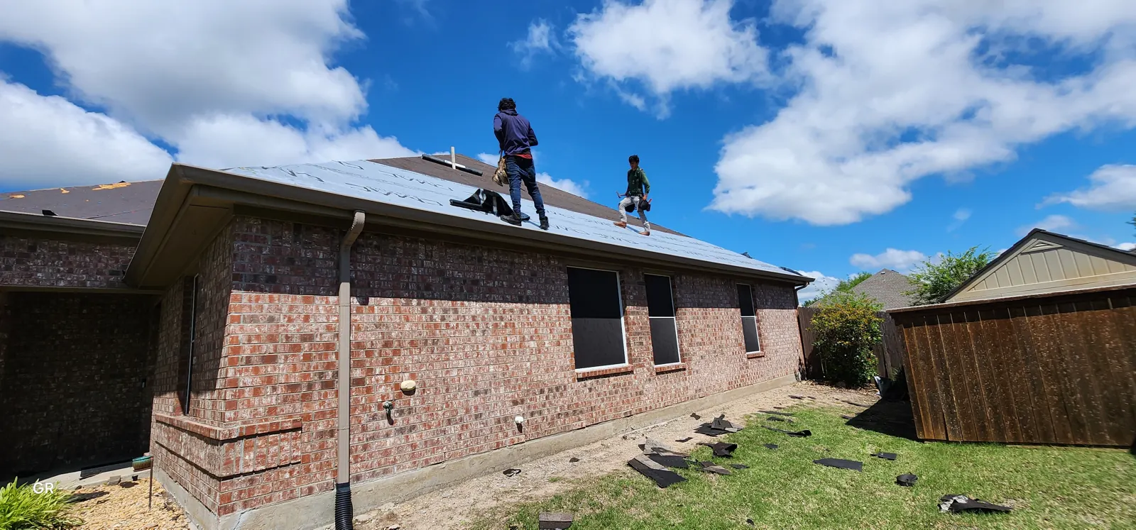 Two roofers laying underlayment on a single-story brick home