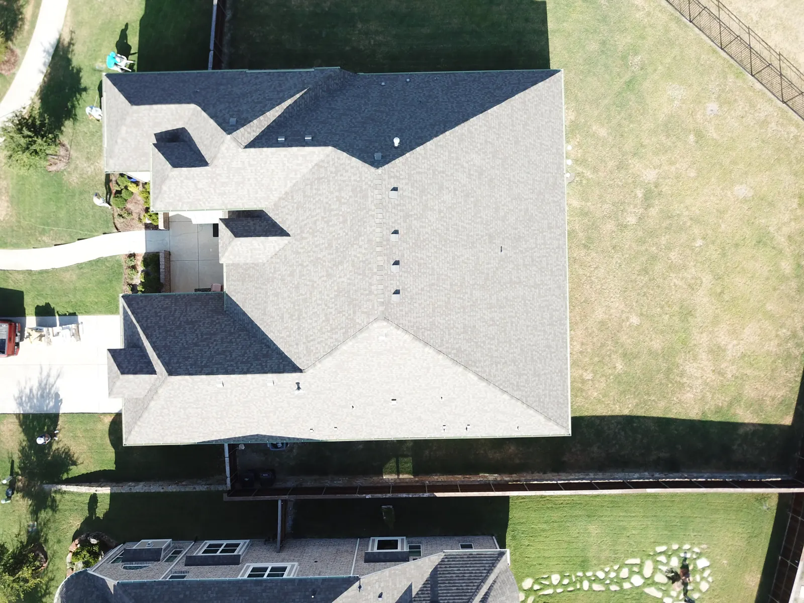 Top-down drone view of a finished architectural shingle roof on a large hip-roof home