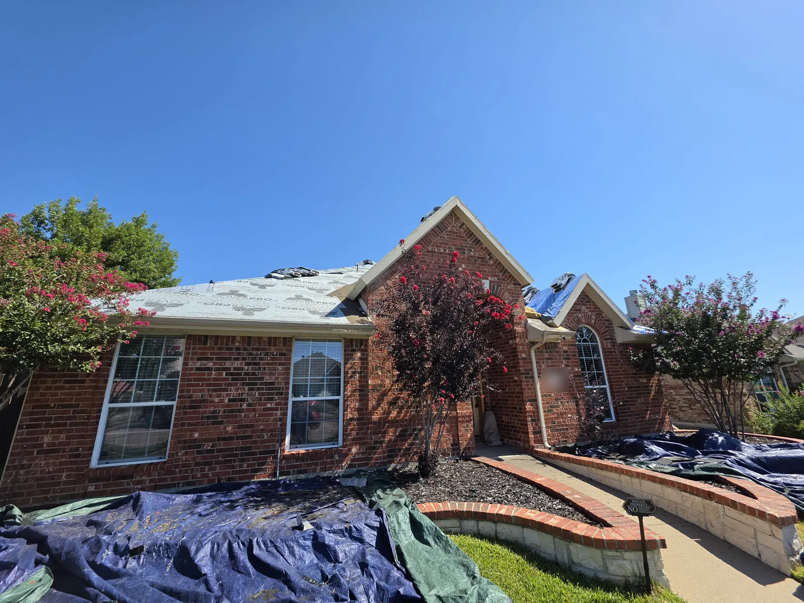 Brick home mid re-roof with synthetic underlayment on the deck and tarps protecting the flower beds