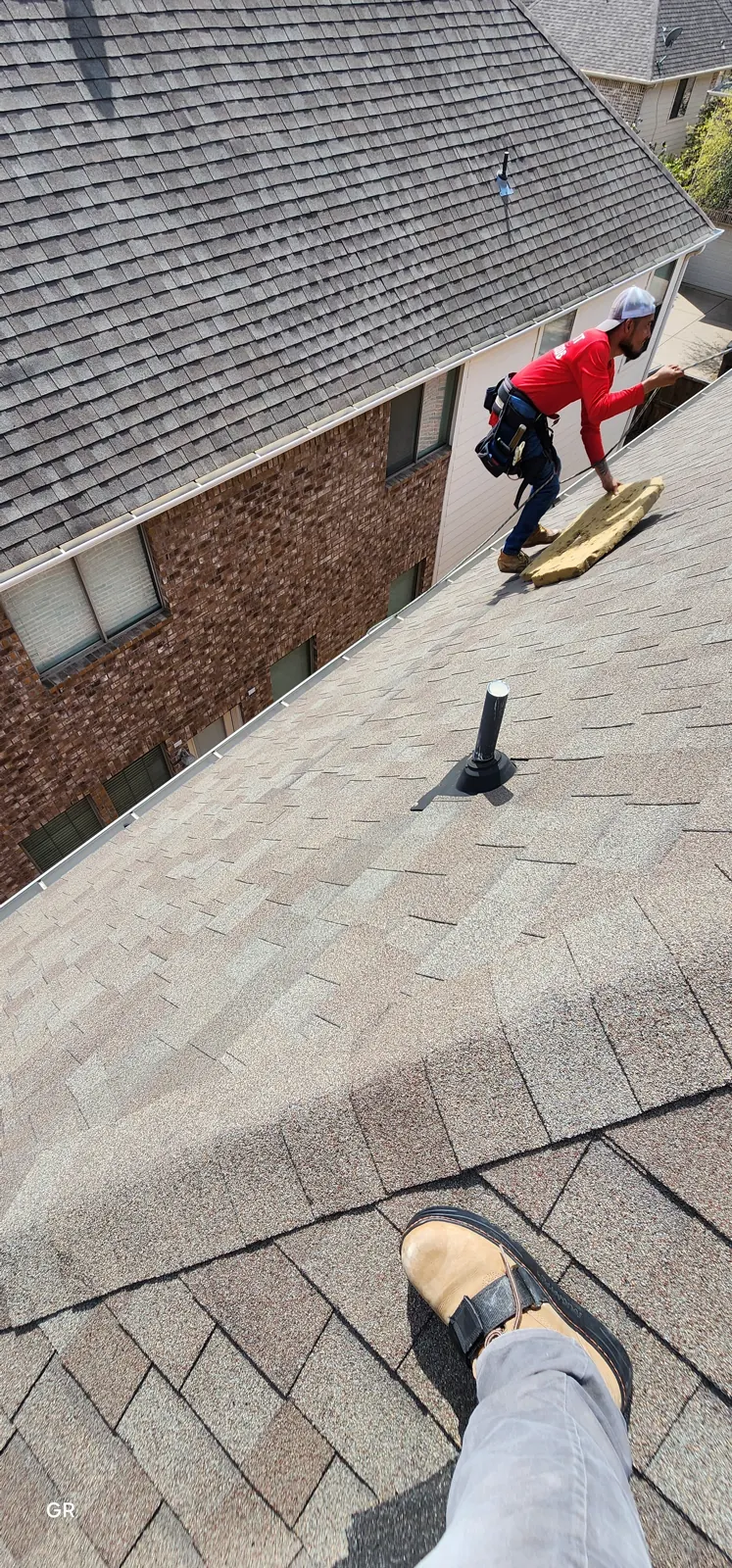 Roofer checking an existing shingle roof beside a two-story brick home