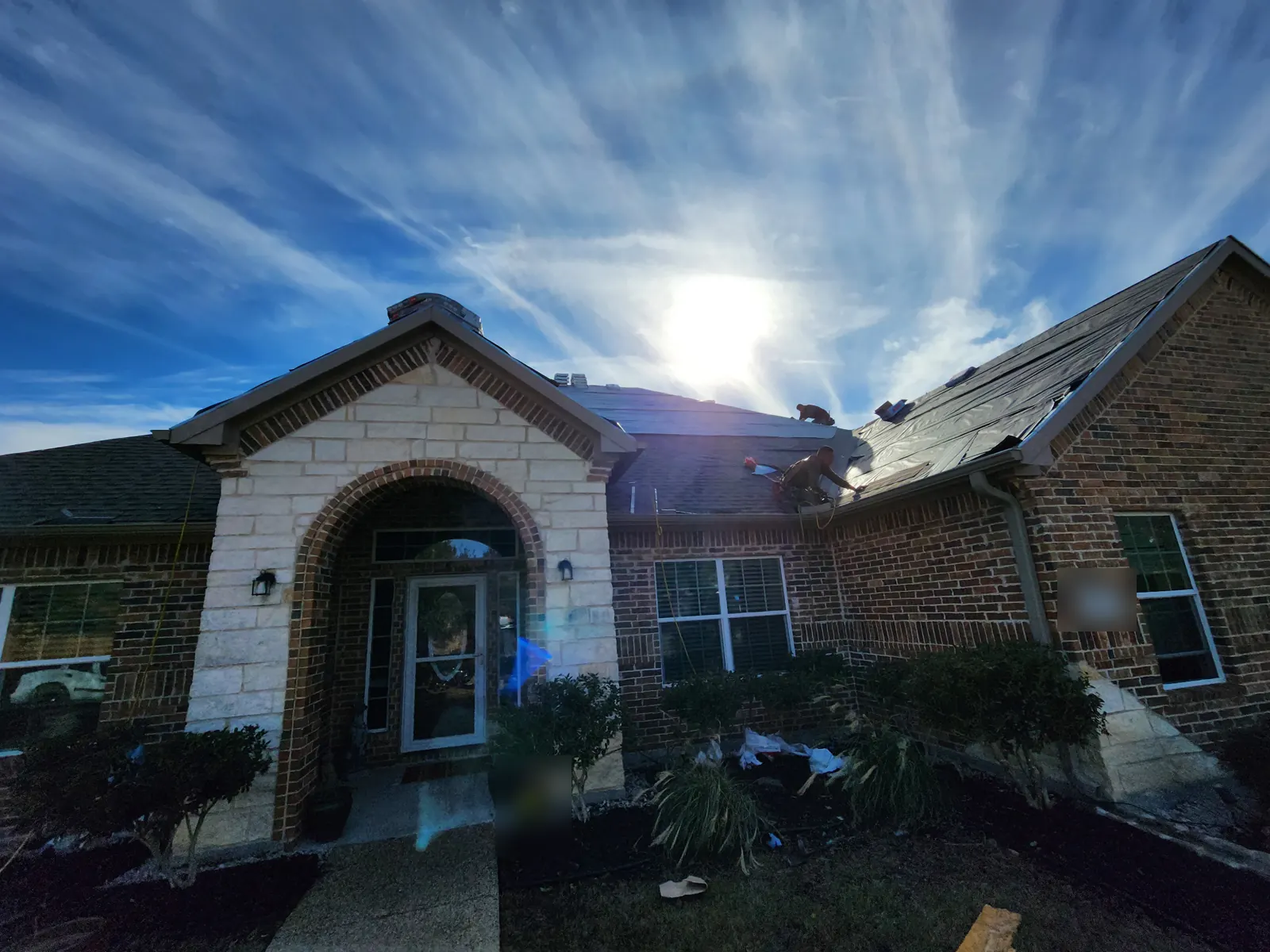 Roofer installing underlayment on a brick home with a stone entry arch