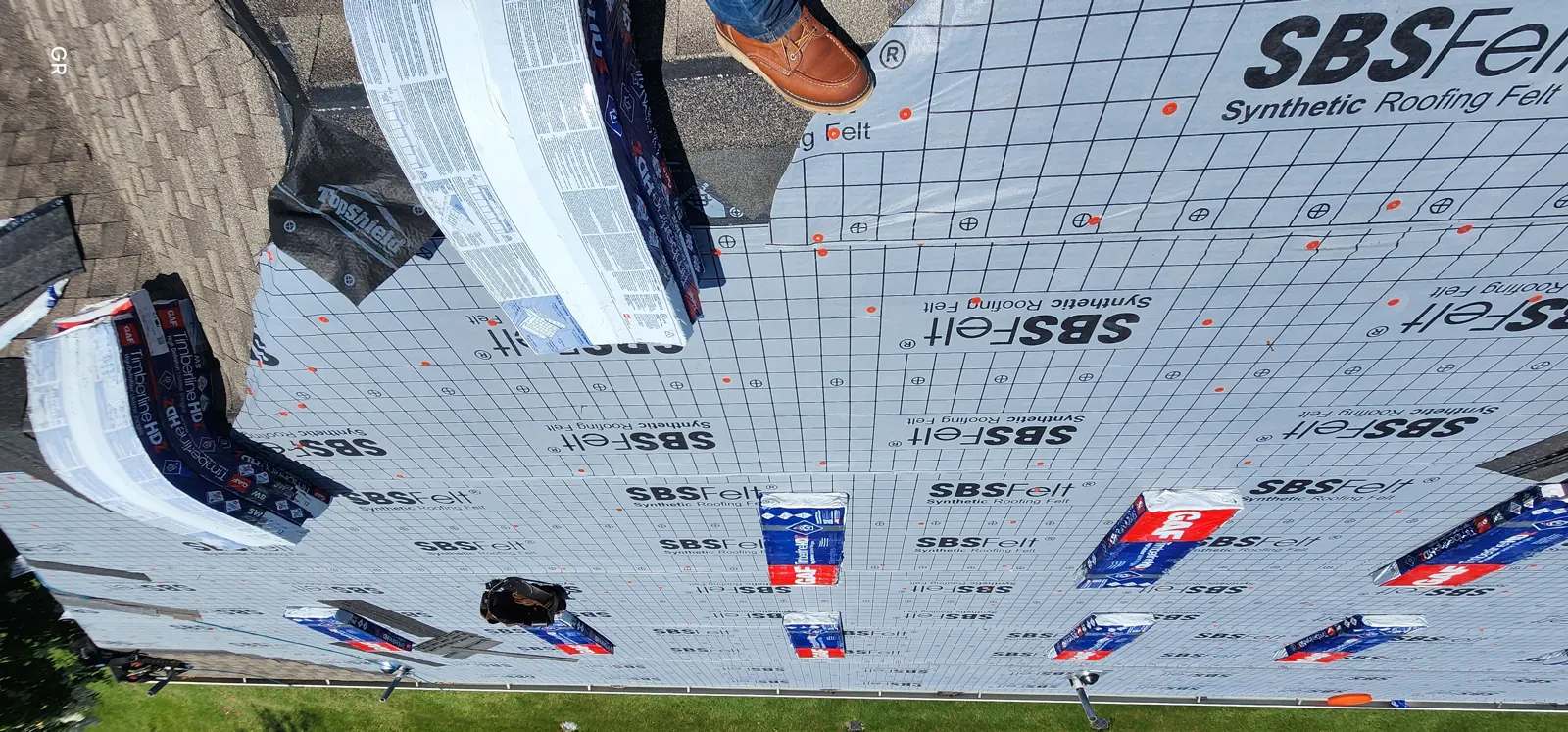 Roof deck covered in synthetic felt with shingle bundles staged across the slope
